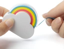 A white cloud-shaped memo tape dispenser with colourful rainbow tape being pulled out by a hand.
