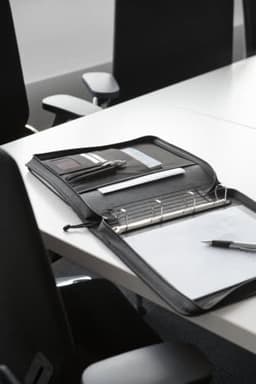 A black polyester folder open on a white table, featuring a notepad, pens, and a binder mechanism inside.