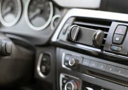 A black ABS mobile phone holder mounted on a car dashboard near the air vents, with various control buttons visible.