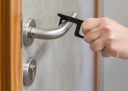 A hand holding a black aluminium door opener, interacting with a door handle. Metal door fixtures are also visible.