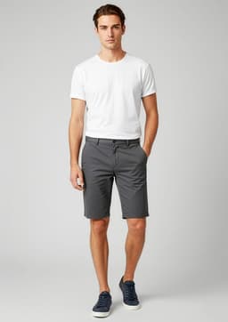 A model wearing grey dress shorts paired with a white t-shirt and navy shoes, featuring a branding logo.