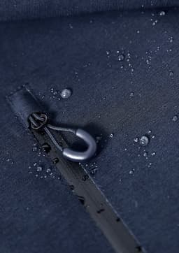 A navy blue rain jacket with water droplets on the fabric, featuring a zipper and a branding label.