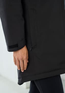 A black unisex rain jacket featuring a hand elegantly positioned near the hem, demonstrating its sleek design.