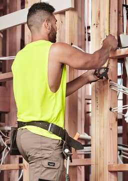A man wearing a fluorescent yellow sleeveless tee is working with tools in a construction setting.