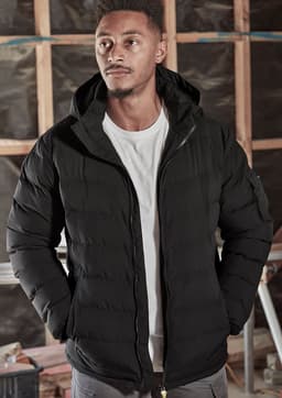 A black unisex hooded puffer jacket with a zip front, worn by a model in a construction setting.