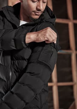 A black unisex puffer jacket with a hood, featuring a zip-up front and a pocket on the arm.