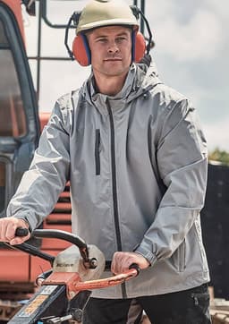 A man wearing a light grey unisex packable rain jacket, with a helmet and ear protection, operating machinery outdoors.