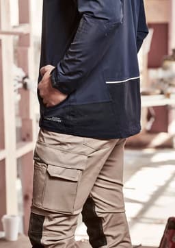 A navy unisex waterproof jacket is worn by a person with their hand in their pocket, paired with beige cargo pants.