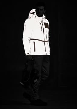 A reflective waterproof jacket in white, featuring a hood, zip pockets, and a logo, displayed on a model in a dark setting.