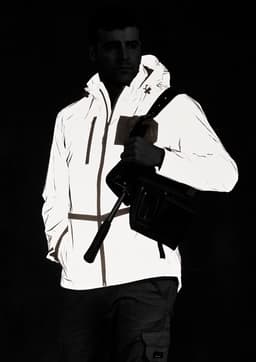 A reflective waterproof jacket in white, featuring a hood and pockets, worn by a model holding a bag.