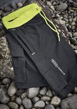A pair of black sports shorts with a neon yellow waistband and drawstring, featuring a logo.