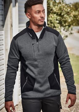 A man wears a grey and black Unisex Streetworx Reinforced Knit 1/2 Zip Pullover, featuring a zippered pocket and side pockets.