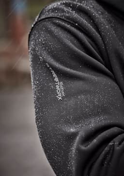 A close-up of a black water-resistant hoodie with a logo on the sleeve, featuring droplets of water on the fabric.