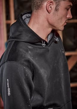 A black unisex water-resistant hoodie with a grey interior and a logo on the sleeve, worn by a man.