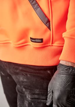 An orange water-resistant hoodie with a logo and a diagonal black detail, paired with black pants and gloved hands.