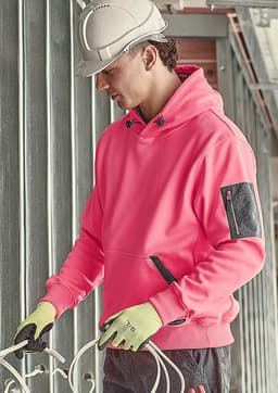 A pink unisex water-resistant hoodie with a pocket, worn by a person in a hard hat and gloves, in a construction setting.