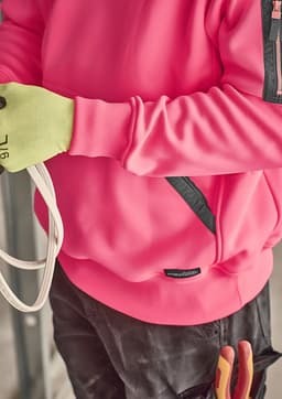 A unisex water-resistant hoodie in bright pink with black accents, worn by a person holding rope and wearing gloves.