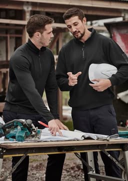 Two men in black, unisex merino wool mid-layer pullovers are discussing plans at a construction site.