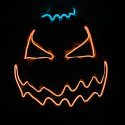 A Halloween pumpkin mask featuring glowing orange and blue accents, with a menacing expression.