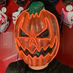 A pumpkin-shaped mask with an angry expression, featuring bright orange and green colours, illuminated with LED lights.