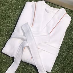 A white cotton unisex bathrobe, featuring a textured fabric and a contrasting trim, neatly tied with a belt.