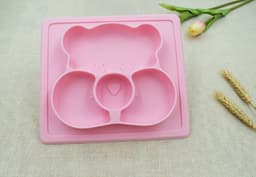 A pink non-slip children's plate featuring a bear design with three compartments, accompanied by a flower and decorative elements.