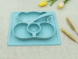 A non-slip children's plate in teal, featuring three compartments and a matching spoon, with a floral background.
