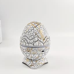 A cracked white and gold egg-shaped projector with buttons at the base sits on a flat surface.