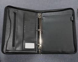 A black ring binder with multiple pockets, a zippered compartment, and a silver metal ring mechanism.