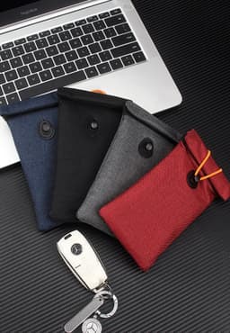 A collection of Faraday Bags in navy, black, grey, and red, beside a car key, set on a laptop background.