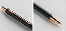 A metal push-up pen in black with a rose gold clip and tip, featuring a textured grip and branding.