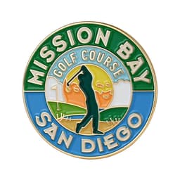 A circular golf ball marker featuring green, blue, and orange colours, depicting a golfer and a sunset. It includes a logo.