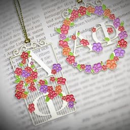 A decorative gold etched ornament featuring floral designs in pink, purple, and orange, with intricate detailing and a logo.