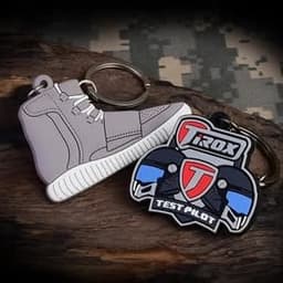 A grey sneaker-shaped keychain and a black and red motorcycle-themed keychain, both featuring metal keyring attachments.
