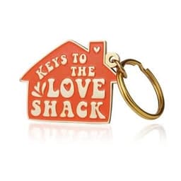 A soft enamel keychain in the shape of a house, featuring orange and gold colours with a logo.