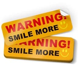 Two rectangular bumper stickers in bright yellow, featuring a smiley face and the text "WARNING! SMILE MORE" in red and black.