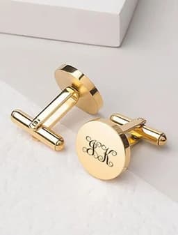 A pair of custom engraved gold cufflinks with a circular design and a decorative monogram.