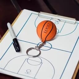 An orange basketball stress reliever keychain on a clipboard with a basketball court diagram, alongside a black marker.