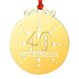 A gold custom die struck ornament featuring a decorative design, with a red ribbon attached.