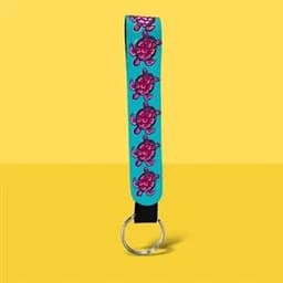 A turquoise neoprene wristlet keychain lanyard featuring pink turtle designs and a metal ring.