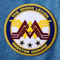 A circular embroidered patch featuring a multicoloured design with yellow, red, and white elements and a blue border.