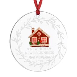A clear acrylic ornament featuring a red and white gingerbread house design, framed by a decorative wreath and ribbon.