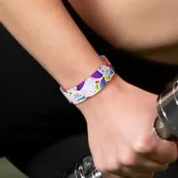 A colourful Tyvek paper bracelet featuring a bright, patterned design worn on a wrist holding a dumbbell.