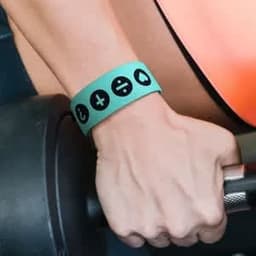 A turquoise wristband with black symbols, worn on a hand gripping a weight. It has a logo on it.