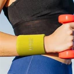 A green terry sweatband wristband with an embroidered logo is worn on a wrist, alongside a pink dumbbell.
