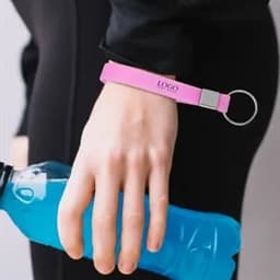 A pink silicone wristband keychain is held by a hand gripping a blue drink bottle. The wristband includes a logo.