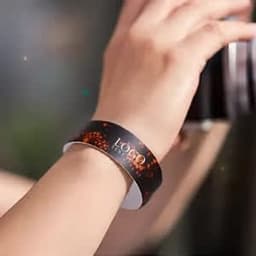 A black PVC waterproof wristband with a logo, positioned on a person's wrist.