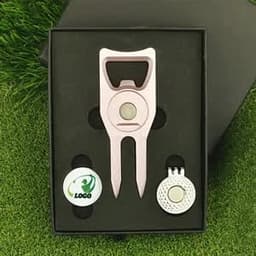 A gift box set featuring a pink cap clip, a ball marker, and a circular marker, presented on a grass background.