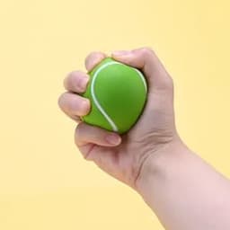 A green tennis stress ball being squeezed by a hand against a yellow background. It features a white seam detail.