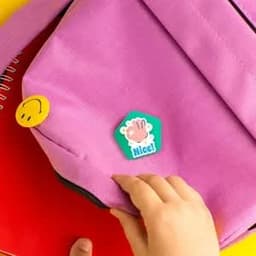 A purple bag features a green and pink pentagonal custom button, along with a yellow smiley face sticker.